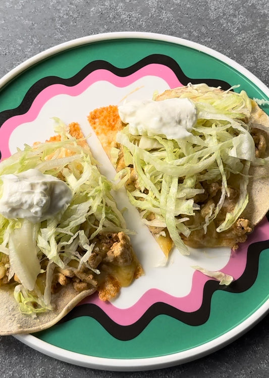 two soft tacos loaded with shredded lettuce and yoghurt on a green and pink plate