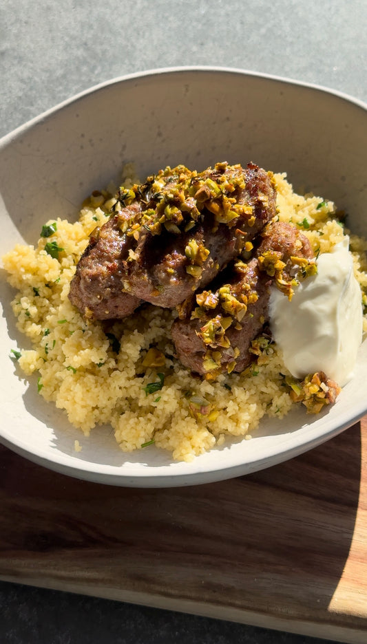 cream bowl sitting on a wooden chopping board is filled with lemon couscous and lamb meatballs dolloped with greek yoghurt.