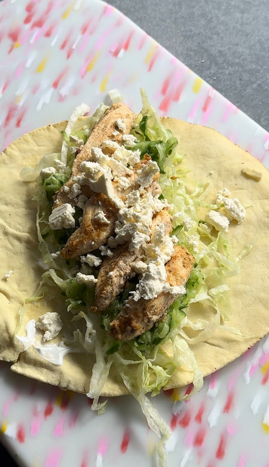 Pita bread wrap on a pink chopping board. Wrap is loaded with greek yoghurt, lettuce, grated cucumber, grilled chicken and crumbled feta.