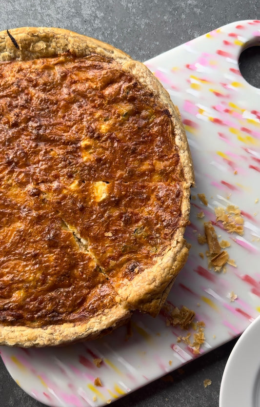 Whole zucchini quiche sitting on pink speckled chopping board. 