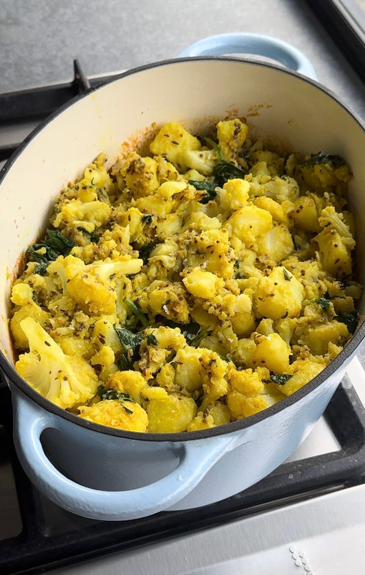 Light blue oval cast iron pot filled with vegetarian curry and topped with a potato and cauliflower mixture. Pot is sitting on a silver stovetop.