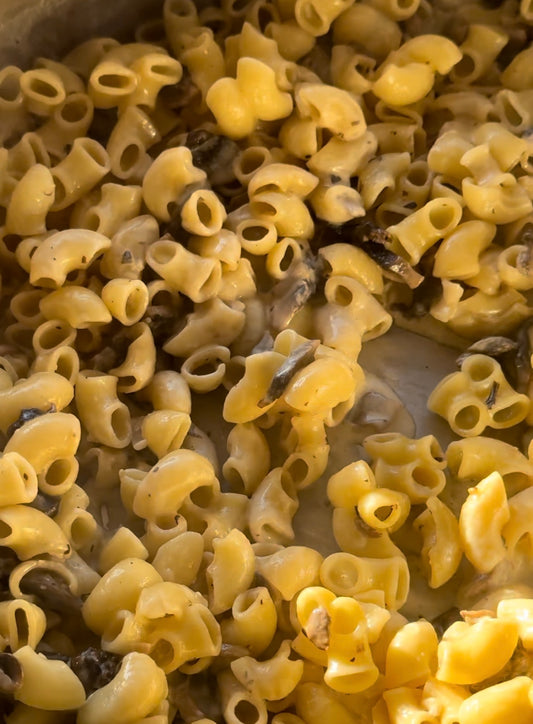 close up shot of elbow pasta with sautéed mushrooms and garlic in a creamy sauce sitting in a large skillet