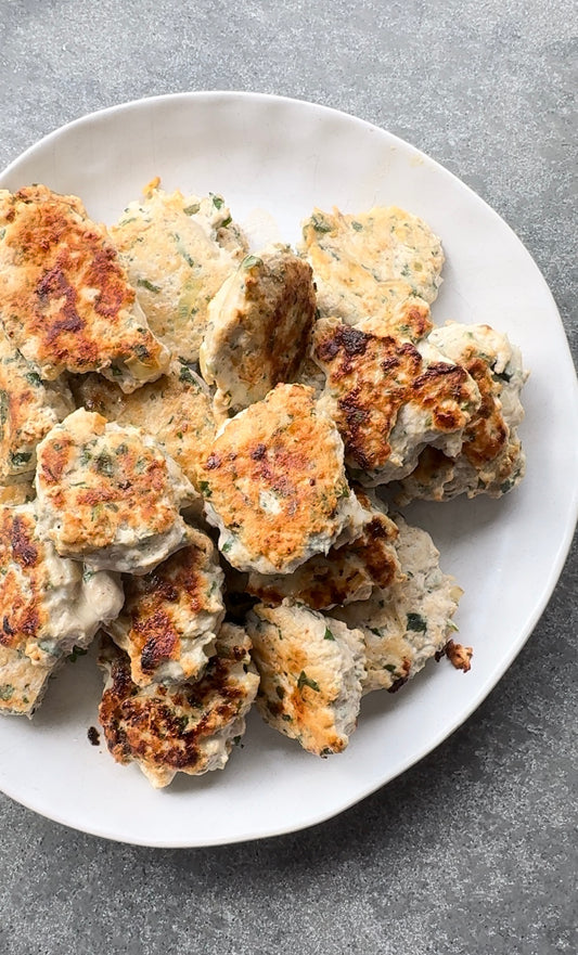 white plate on gray bench top with a stack of medium sized grilled chicken meatballs.