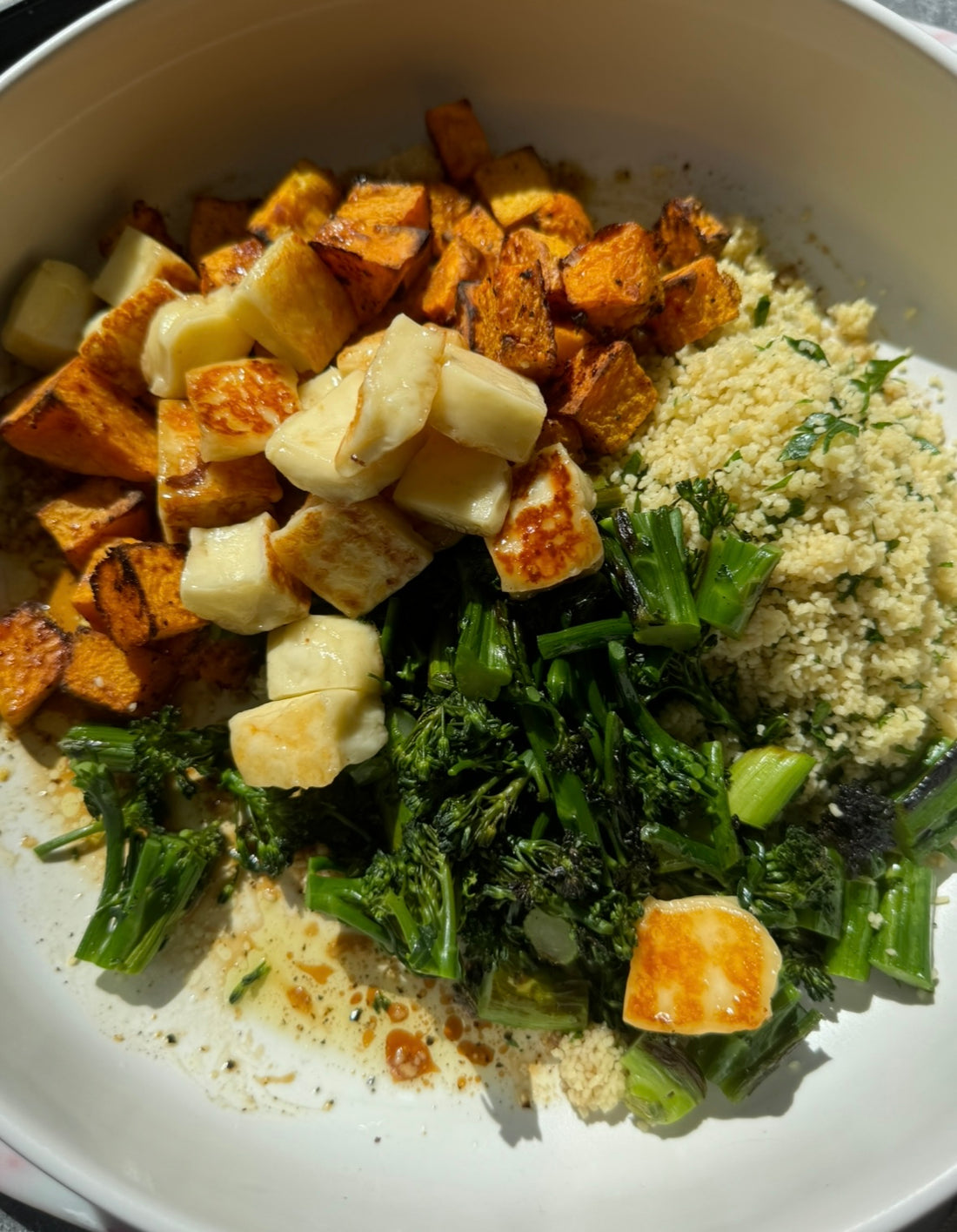 close up of salad bowl filled with couscous, roast pumpkin, chopped charred broccolini and honey seared halloumi before the salad has been tossed.