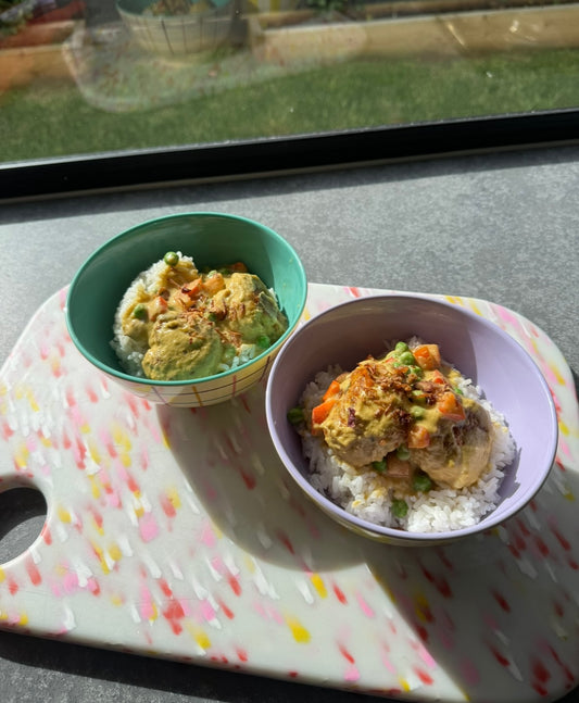 two bowls of rice and curry sitting on a speckled pink chopping board in a kitchen with a window splashback. 