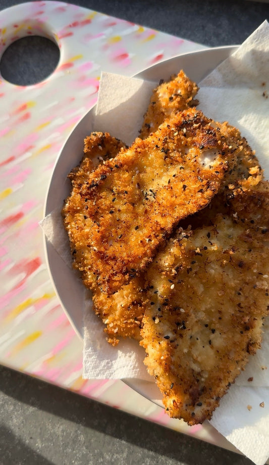 plate of chicken schnitzel on a white plate sitting on a pink speckled chopping board in the dappled sunshine.