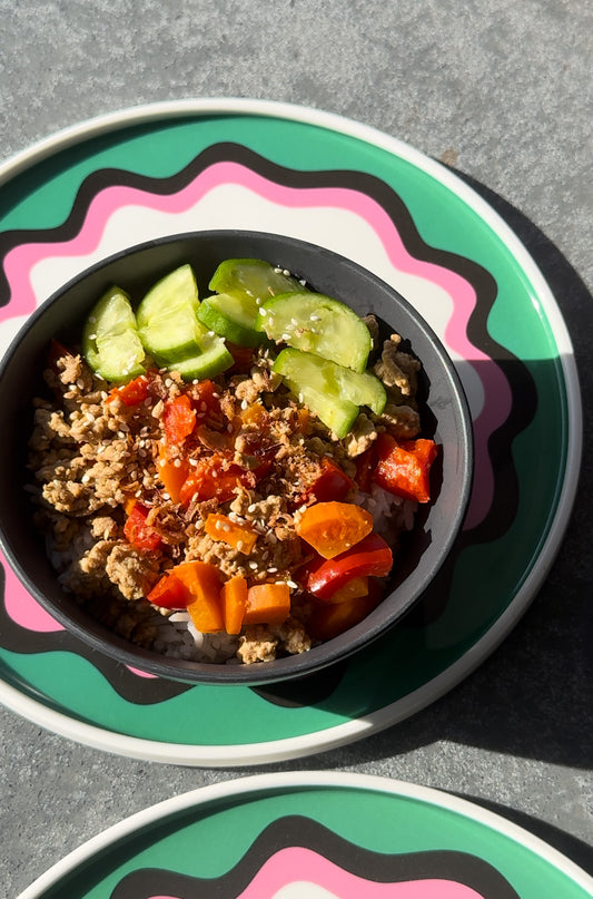 Bowl of teryiaki pork mince tossed with capsicum and carrot, topped with sliced cucumbers sesame seeds and fried shallots