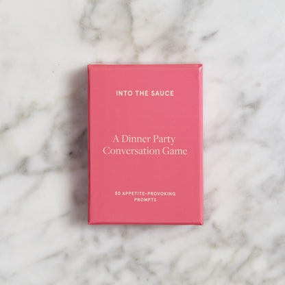 Pink box of dinner party conversation cards on marble table.