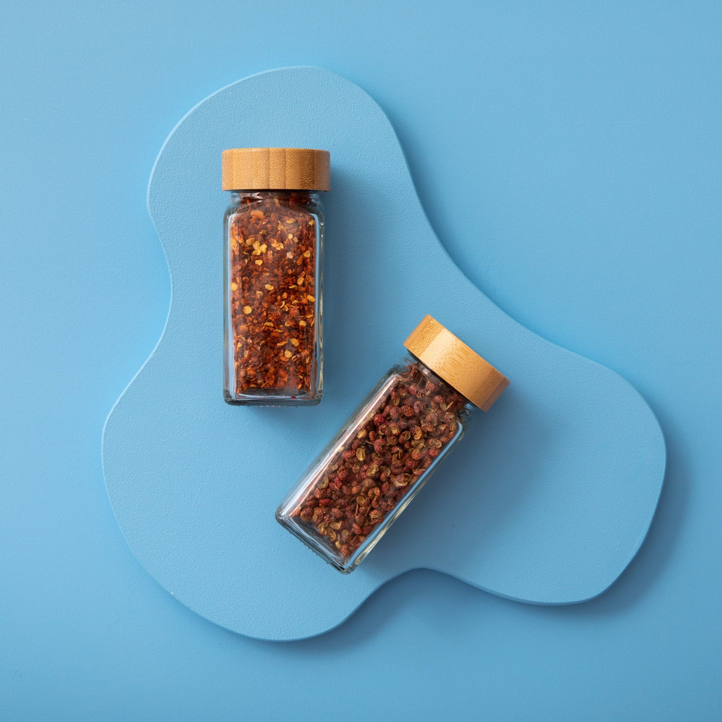 Two glass spice jars with bamboo lids on blue background.